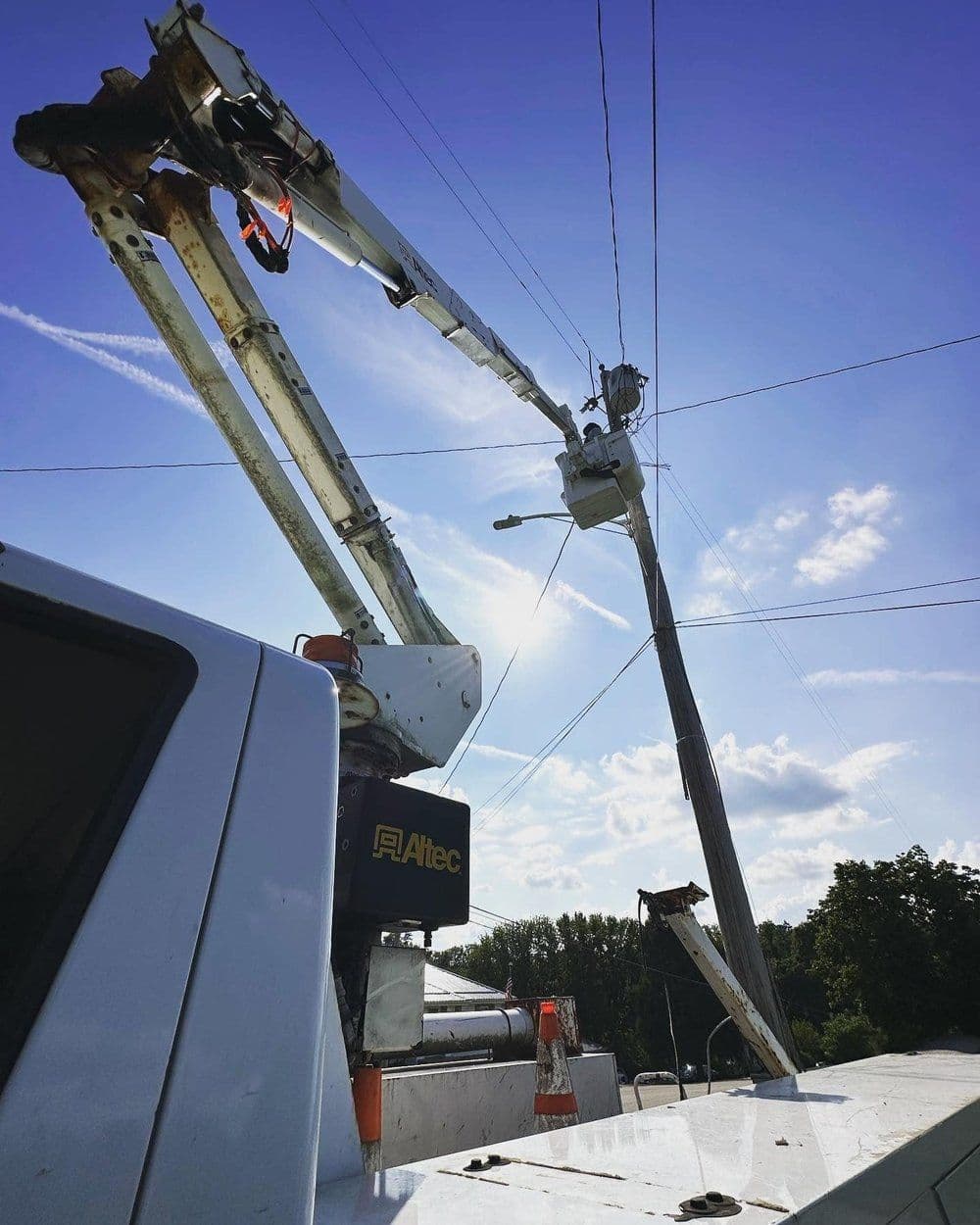 Utility truck with crane repairing power lines against a blue sky.
