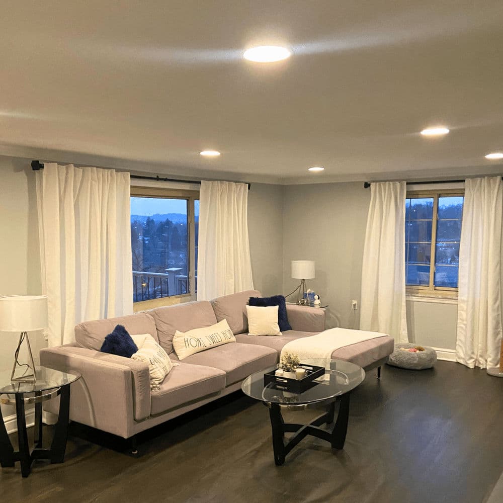 Modern living room with a light gray couch, decorative pillows, and large windows overlooking nature.