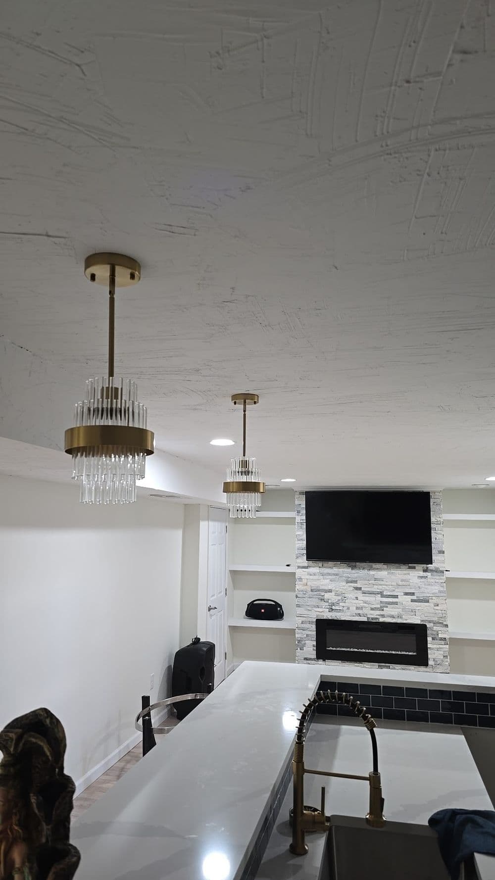 Modern basement interior with pendant chandeliers, stone fireplace, and sleek design.
