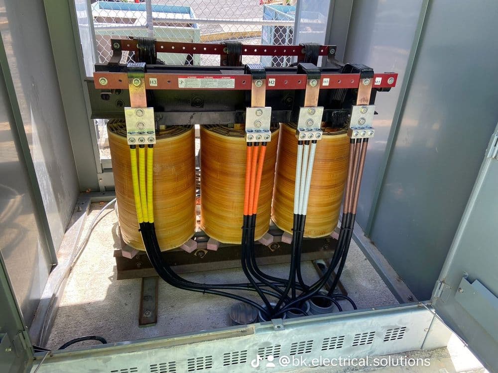 Electrical transformer with yellow coils and cables in a metal enclosure.