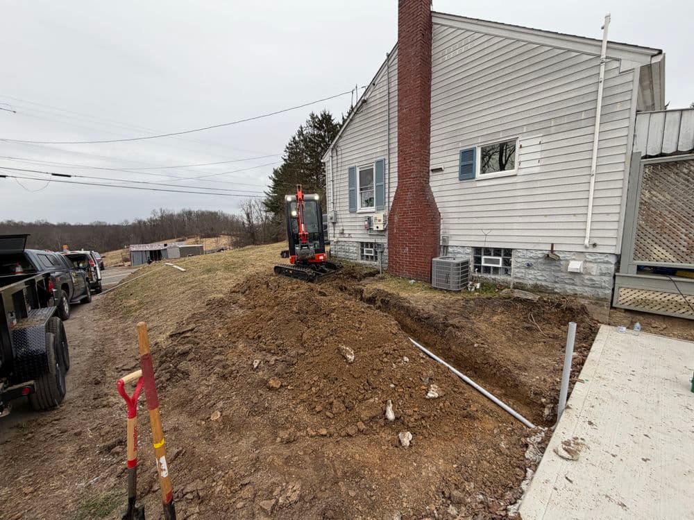Excavation site near house with machinery and freshly dug dirt for utility installation.