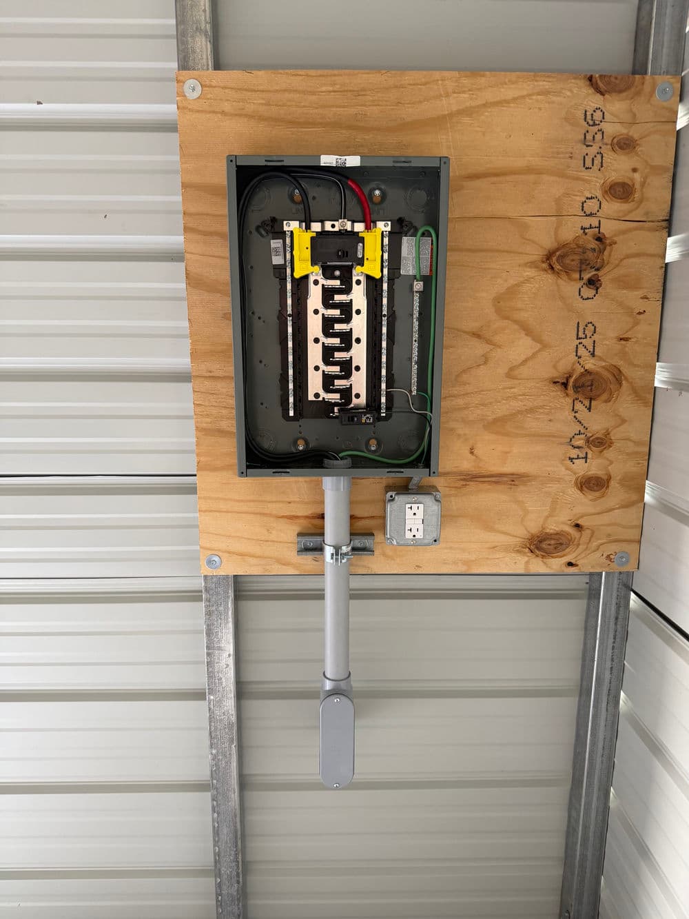 Electrical panel mounted on wood, featuring circuit breakers and wiring in a metal structure.