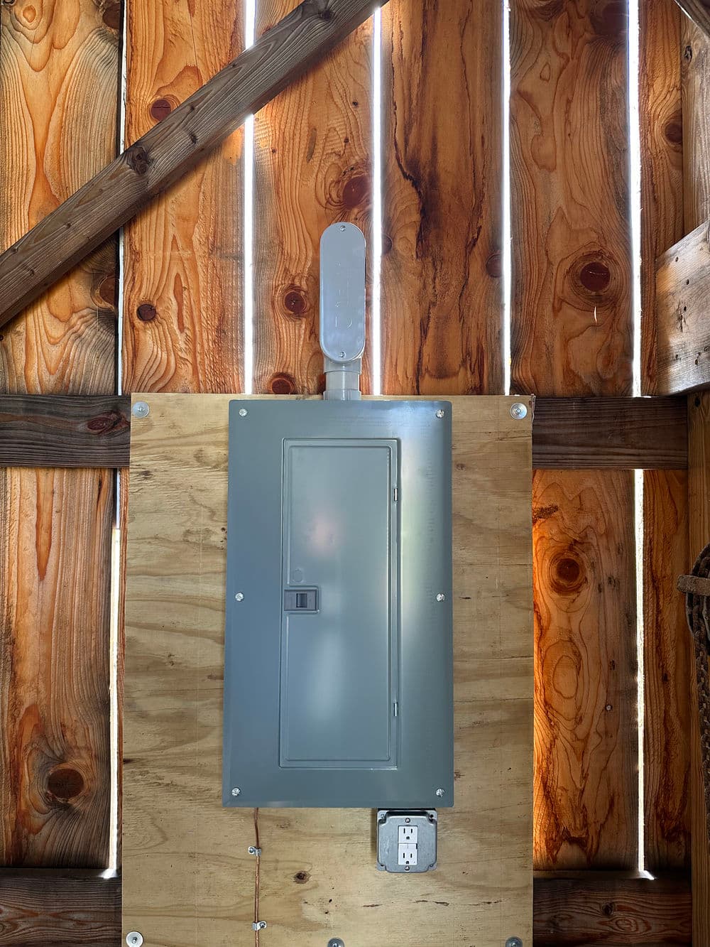 Electrical panel mounted on wooden wall inside a rustic shed with natural light streaming in.