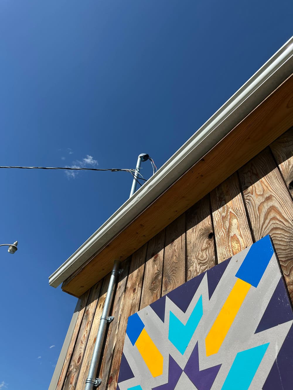 Colorful mural on wooden wall with blue sky and utility pole in the background.