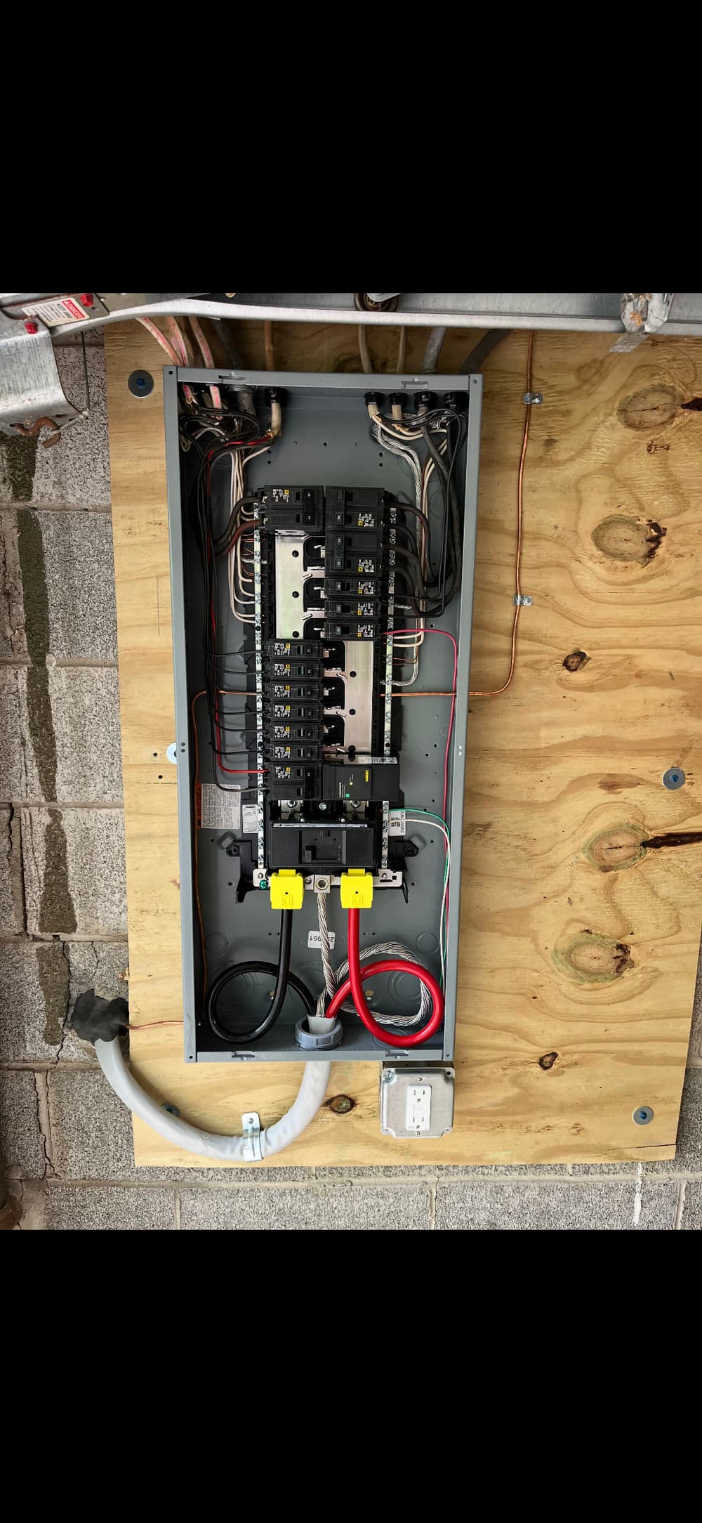 Electrical panel mounted on wooden surface, featuring multiple circuit breakers and wiring connections.