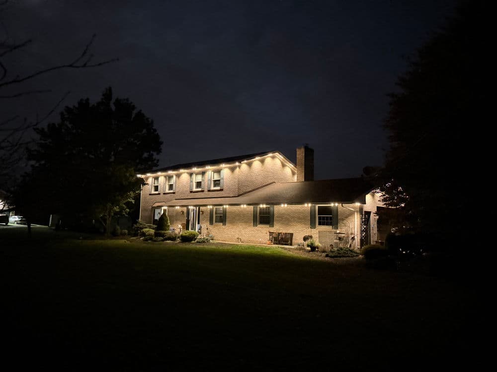 Two-story home illuminated by warm outdoor lights at night, surrounded by a lush lawn.