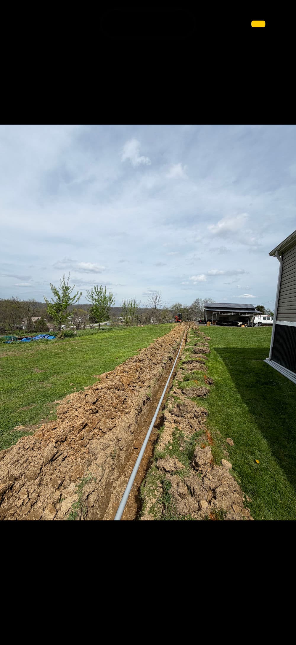 Excavated trench for utility installation in a grassy backyard with house and trees in background.