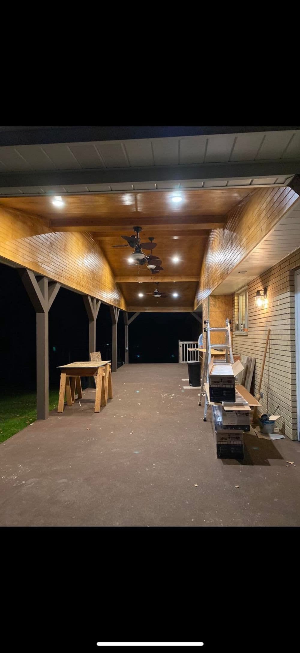 Well-lit outdoor porch with ceiling fans, wooden beams, and tools for home improvement.