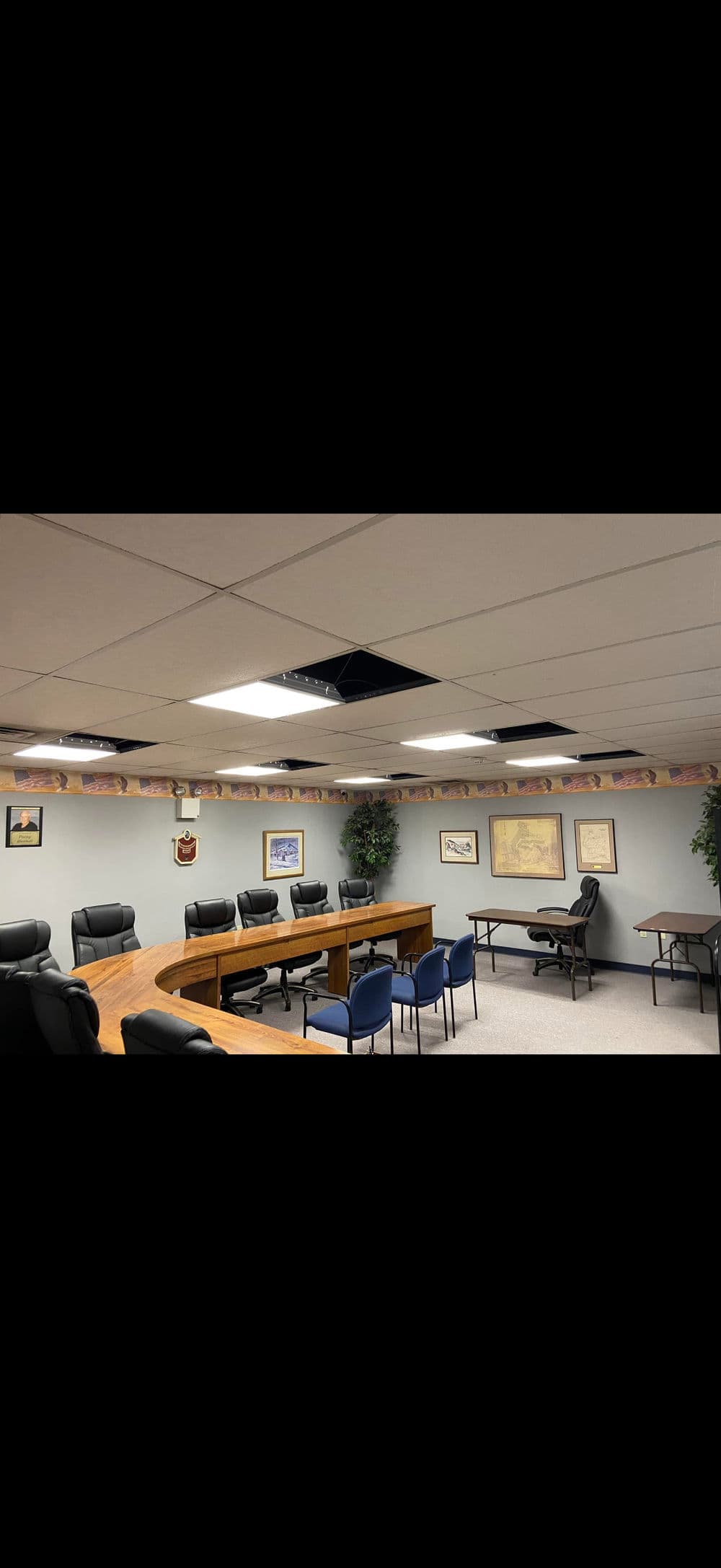 Conference room with wooden table, black chairs, and ceiling repairs visible.