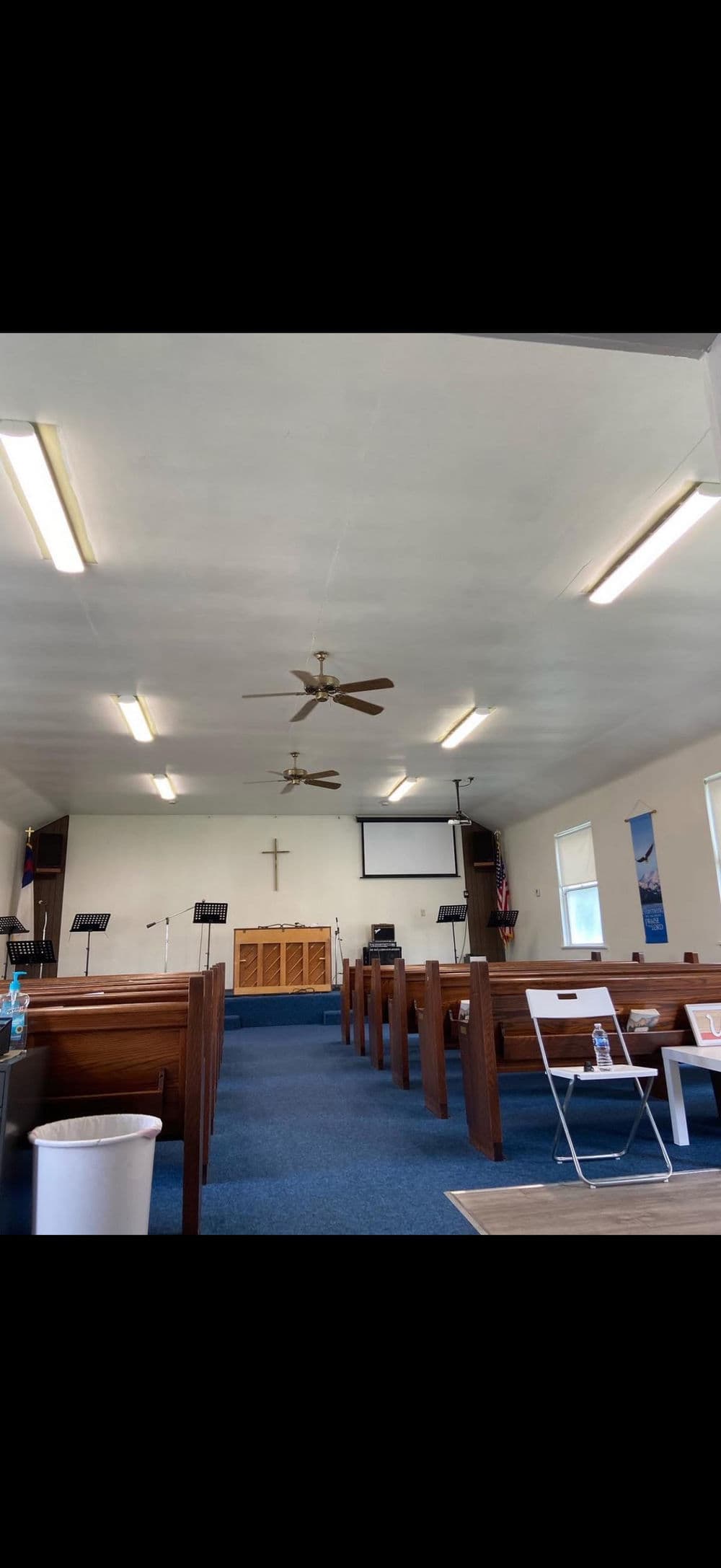 Interior of a church with wooden pews, projector screen, and ceiling fan. Bright and spacious.